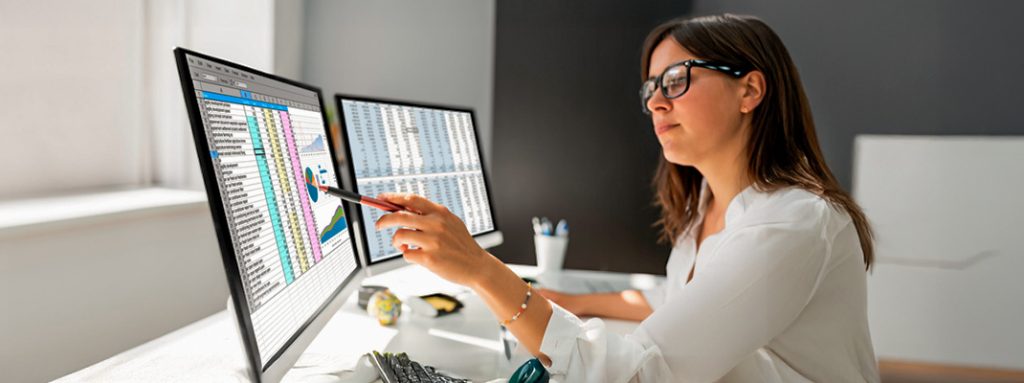 Uma mulher analisa gráficos financeiros em dois monitores, com uma caneta touch na mão. O que é e Como Reduzir a Sinistralidade em OPS.