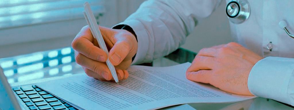 Um médico de jaleco escreve em documentos. Afinal, o que é e Como Funciona a Auditoria Médica?