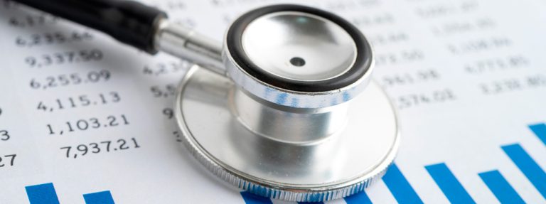 Um estetoscópio sobre papéis com números e gráficos financeiros em um ambiente hospitalar. Curso: Como Conciliar o Conhecimento Técnico e o Impacto Financeiro para Avançar na Melhoria da Prática Clínica em um Hospital.