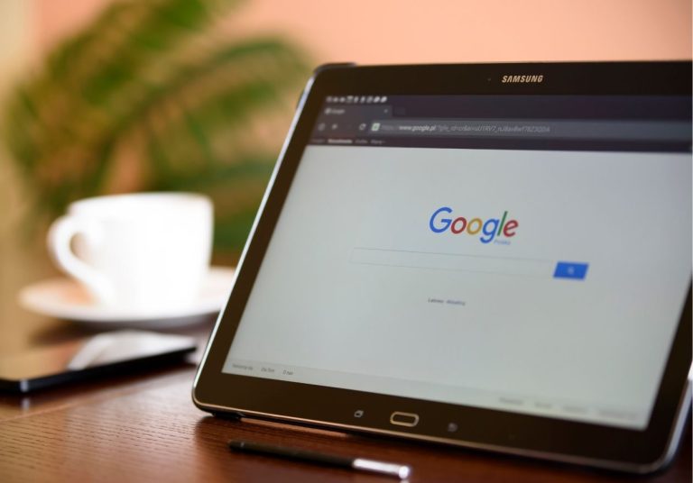 Um tablet exibe a página inicial do Google, com uma xícara de café e celular ao fundo. Curso: Aprenda com os Fundadores do Google.
