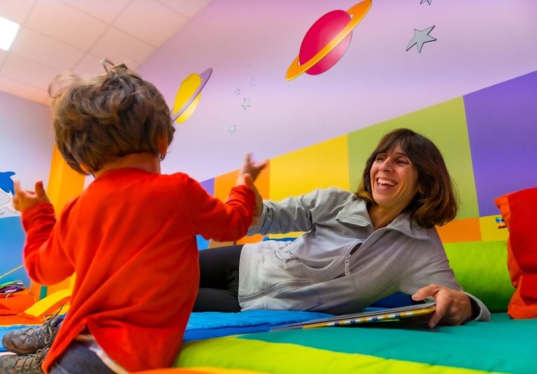 Criança e mulher brincam em sala colorida com tapete e decorações espaciais. Curso: Capacitação em Integração Sensorial - Equipe Multidisciplinar.