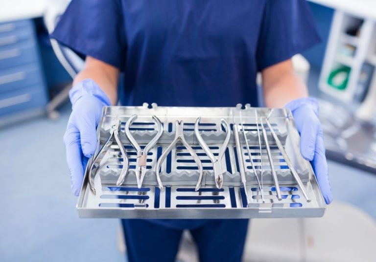Profissional com luvas segura bandeja com instrumentos esterilizados em ambiente médico. Curso: CME - Central de Material Esterilizado.