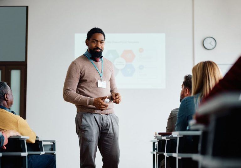 Homem apresenta em sala de aula com projetor, público sentado e atento. Curso: Coach de Carreira.