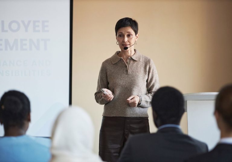 Mulher apresenta em sala com projetor, público sentado e atento. Curso: Coach de Equipes.