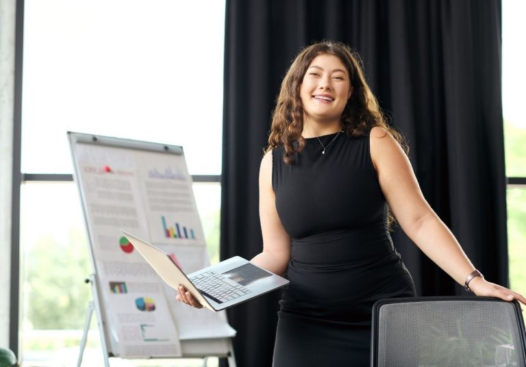 Uma mulher de vestido preto segura papéis e está ao lado de um quadro com gráficos. Curso: Construir uma Imagem Profissional de Impacto.