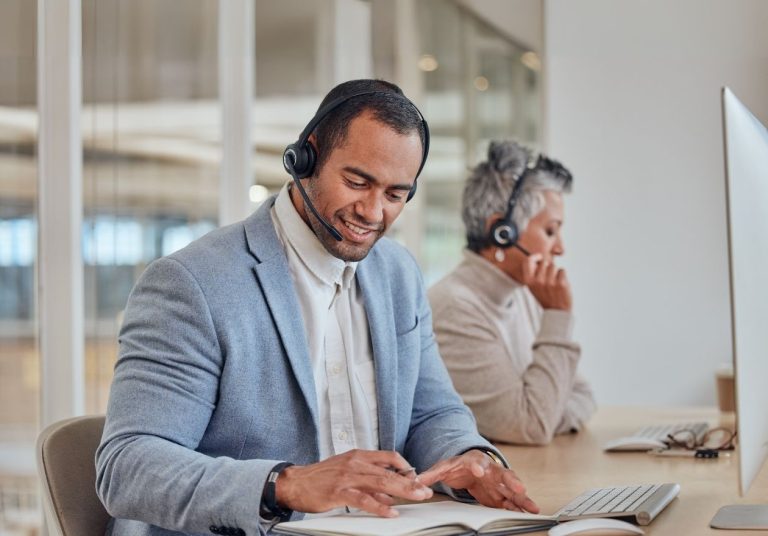 Um homem e uma mulher com headsets trabalham em computadores em um escritório. Curso: Criação de um Serviço de Classe Mundial.