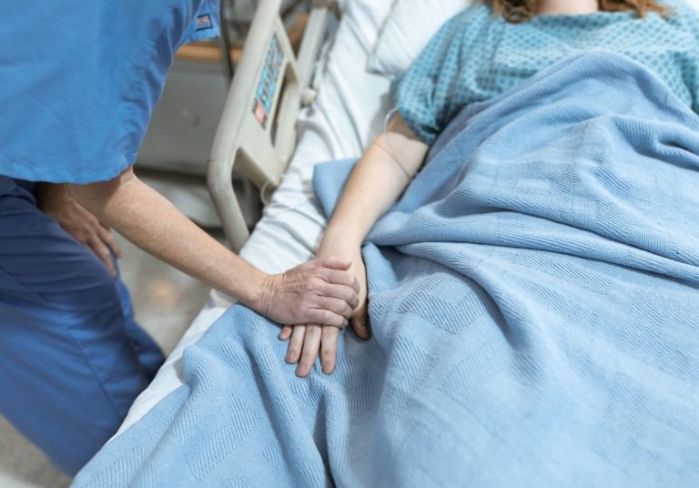 Profissional de saúde segura a mão de um paciente em uma cama hospitalar. Curso: Diagnóstico e Tratamento da Agitação Psicomotora.