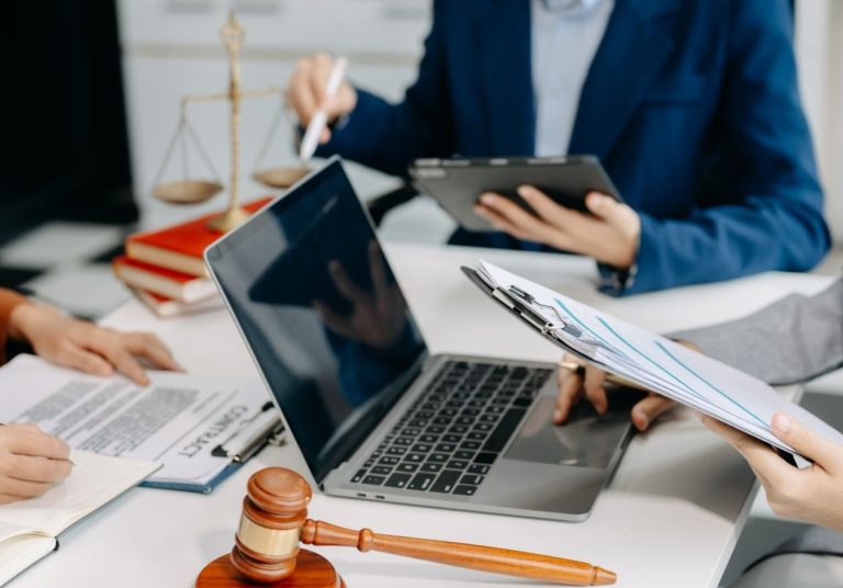 Profissionais analisam documentos e um laptop sobre mesa com um martelo de juiz e uma balança. Curso: Direito Digital na Era dos Dados.