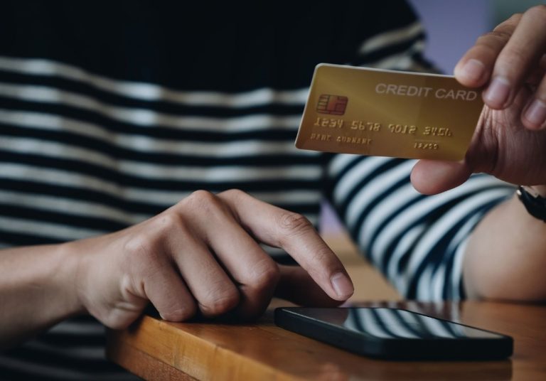 Mão segura cartão de crédito e clica em um celular, realizando uma transação digital. Curso: Direito do Consumidor Foco nas Cooperativas de Crédito.