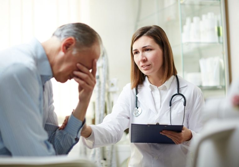 Médica com estetoscópio conversa com um paciente que parece preocupado, em um consultório médico. Curso: Disclosure e Gestão de Conflitos.