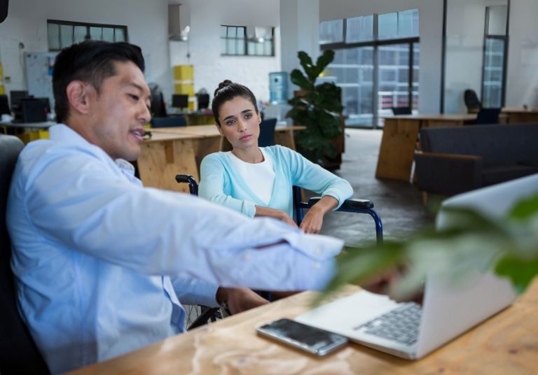 Um homem e uma mulher conversam em um escritório com laptop e plantas. Curso: Endomarketing.