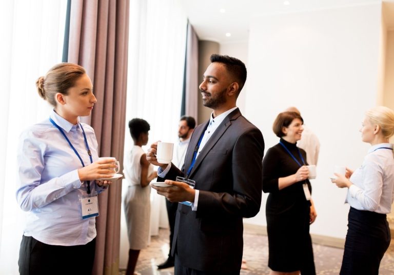 Um grupo de pessoas conversa em um evento, segurando xícaras e portando crachás. Curso: Fazer Networking.