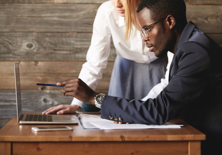 Um homem e uma mulher analisam um laptop sobre uma mesa de madeira. Curso: Focar em Momentos de Pressão.