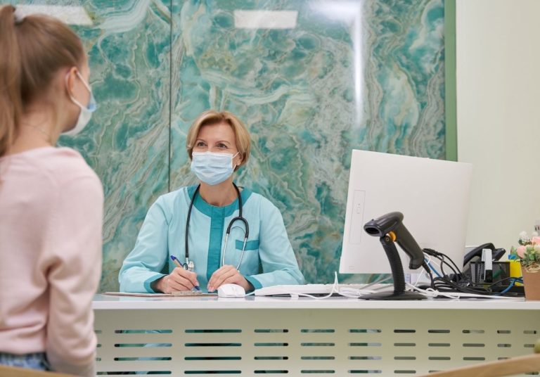 Uma profissional da saúde, usando máscara, atende uma cliente em um balcão. Curso: Formação e Capacitação para DPO com Ênfase na Saúde.