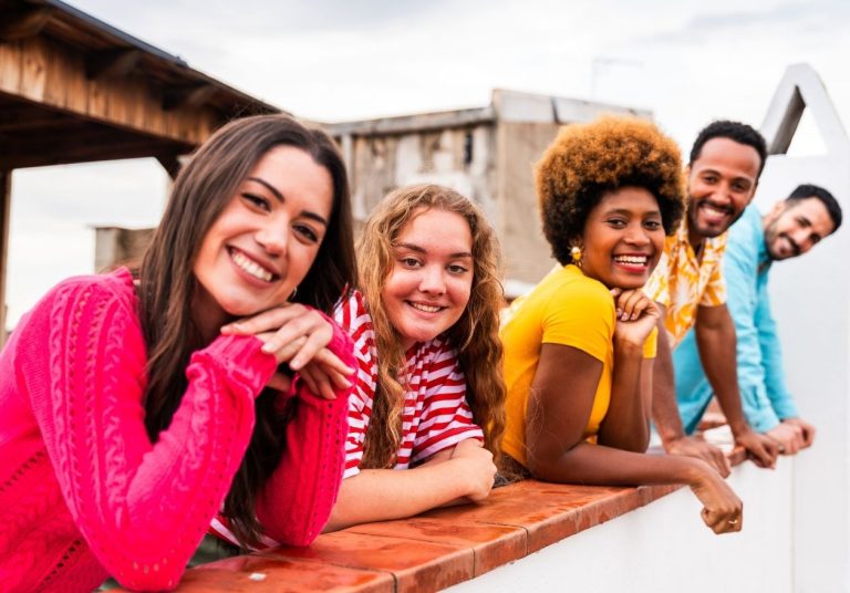 Um grupo de jovens sorridentes apoia os braços em uma mureta ao ar livre. Curso: Geração Y.