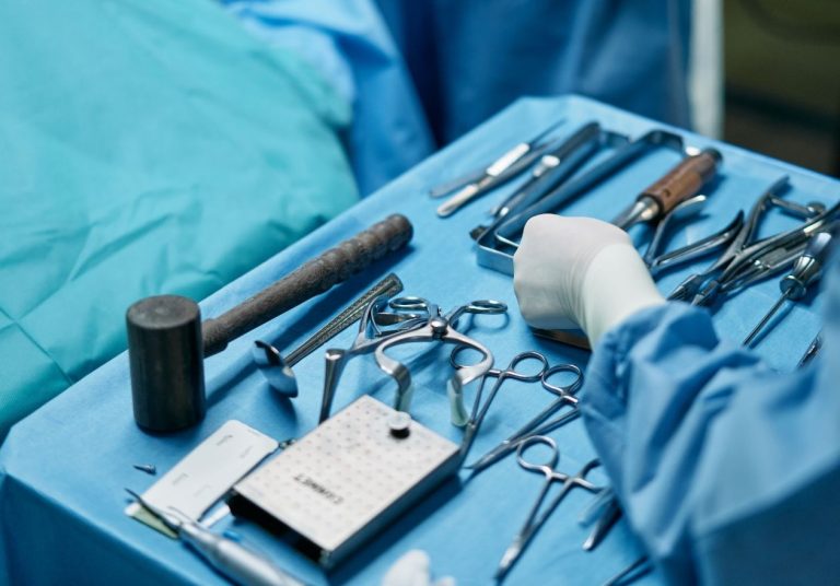 Mesa com instrumentos cirúrgicos e martelo médico, em ambiente hospitalar. Curso: Gestão de Equipamentos.