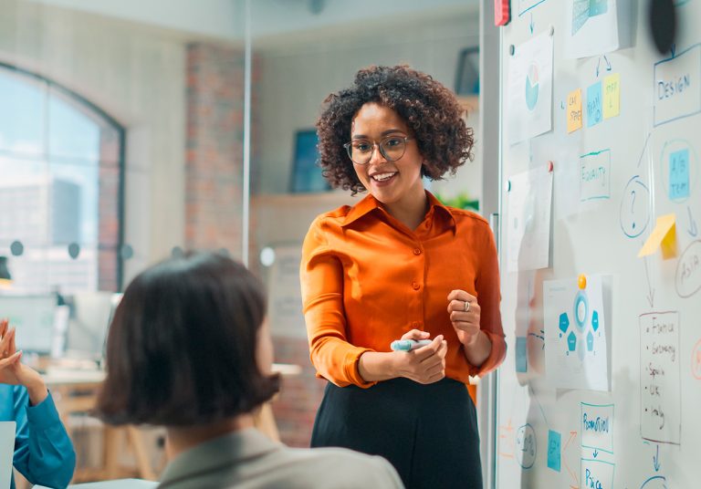 Mulher apresentando ideias sobre liderança e gestão exponencial na saúde, com quadro de anotações e gráficos em um ambiente de escritório.