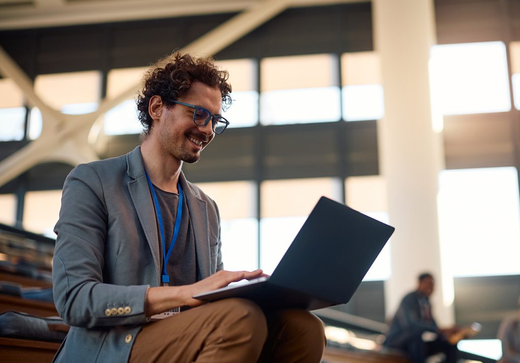 Homem, especialista formado no MBA em Proteção de Dados, Privacidade e Novas Tecnologias Aplicadas à Saúde. Ele olha para um notebook sobre as pernas em um ambiente moderno.