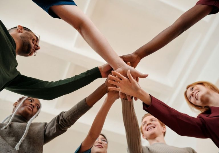 Um grupo de pessoas une as mãos em um círculo, simbolizando união e motivação. Curso: Motivação de Pessoas.