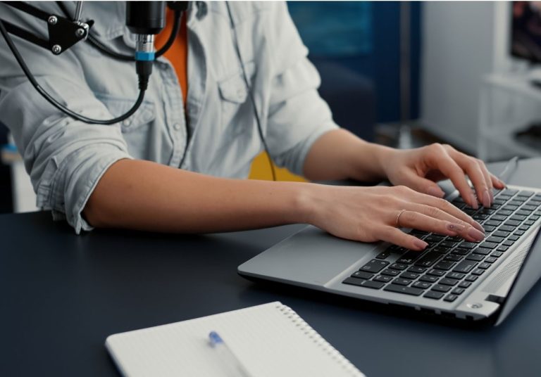 Uma pessoa digita em um laptop, com um caderno ao lado. Curso: Novos Modelos de Negócio.