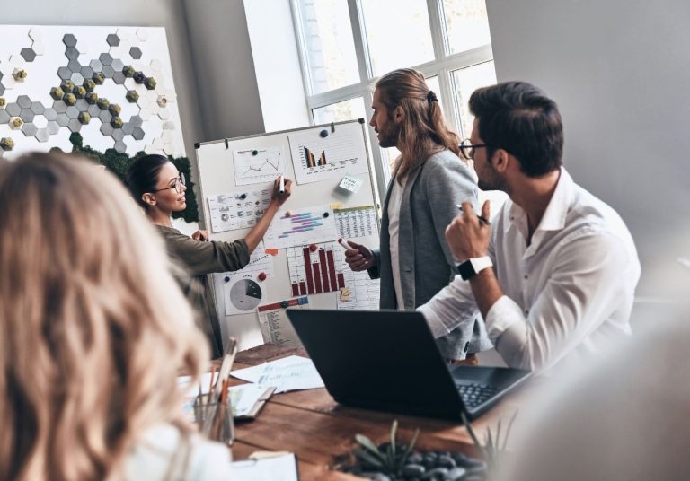 Um grupo de pessoas está de frente para um quadro com gráficos. Curso: Processo e Inovação nas Organizações.