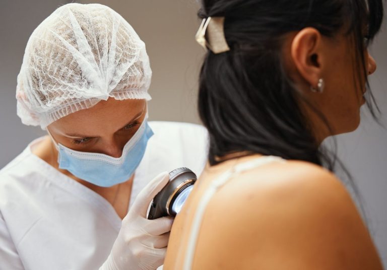 Médica com touca e máscara examinando a pele de uma paciente com um dermatoscope. Curso: Trilha de Aprendizagem: Dermatologia.