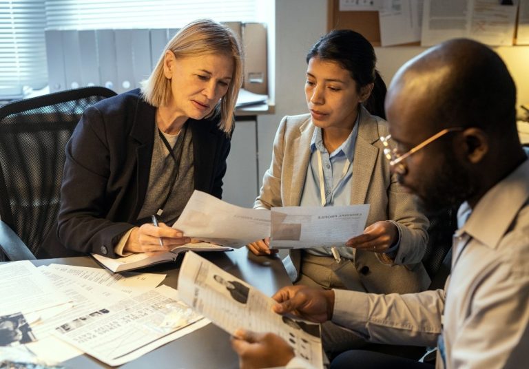 Equipe analisa documentos em reunião, em sala com cadeiras e mesa de trabalho. Curso: Auditoria em Saúde: Gestão e Impactos dos Transtornos Globais do Desenvolvimento.