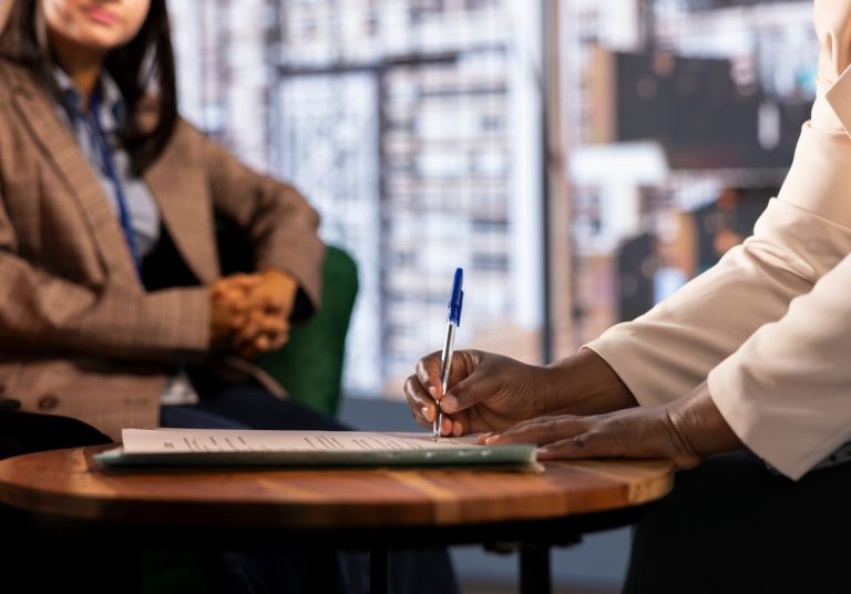 Pessoa assina documento em mesa, outra observa, em ambiente corporativo. Curso: Compliance e Integridade.