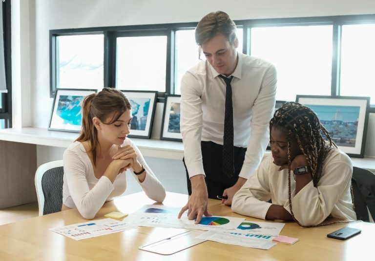 Pessoas analisam gráficos em mesa, em escritório com quadros e janelas. Curso: Compreendendo o IDSS das Operadoras de Saúde.