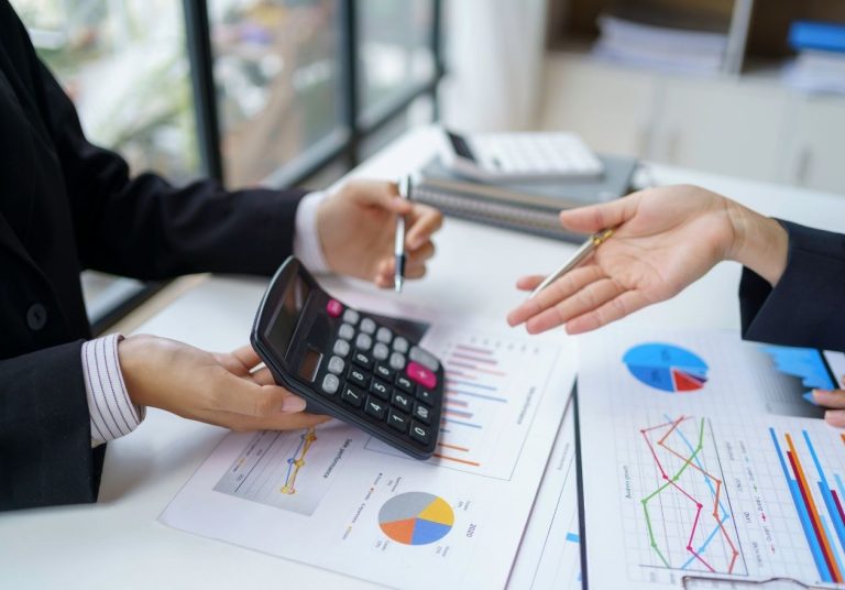 Duas pessoas analisam gráficos financeiros e uma calculadora. Curso: Finanças Cooperativistas em Operadoras de Planos de Saúde.