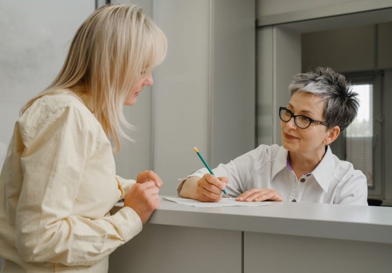 Mulher conversa com atendente em balcão, que anota com lápis em papel. Curso: Intercâmbio.