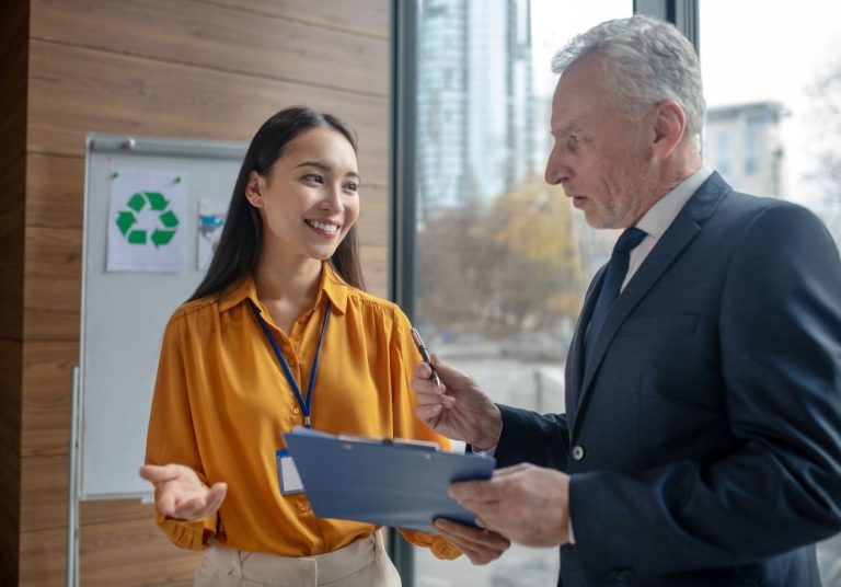 Homem e mulher conversam em um escritório com um símbolo de reciclagem ao fundo. Curso: Mecanismos de Desenvolvimento Limpo.
