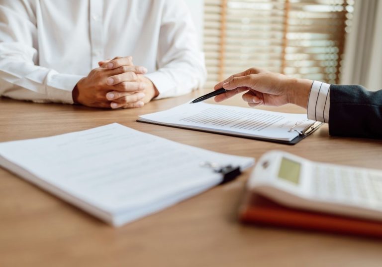 Duas pessoas em reunião, com documentos, caneta e calculadora sobre a mesa. Curso: Regulação dos Planos de Saúde - Produtos.