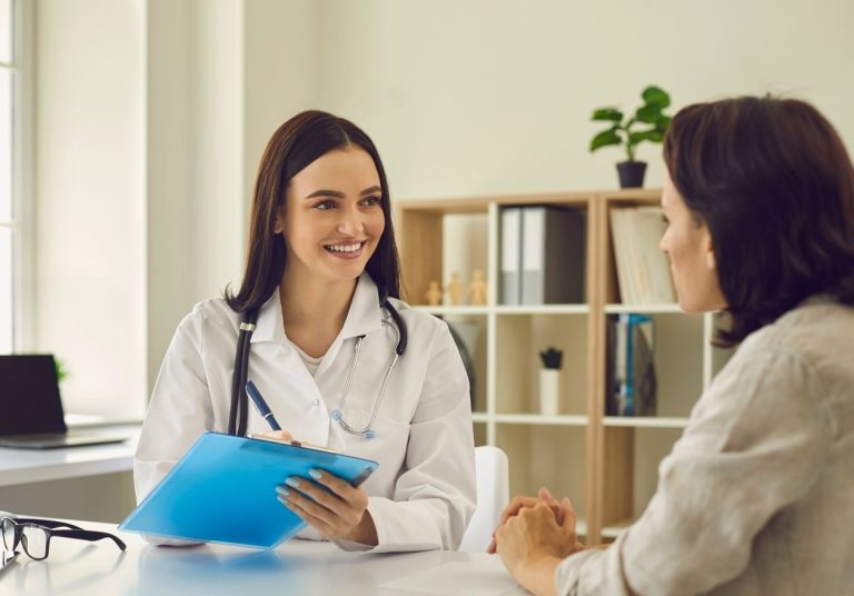 Médica com prancheta conversando com paciente em consultório, com estante ao fundo. Curso: Regulação dos Planos de Saúde - Rede de Prestadores.