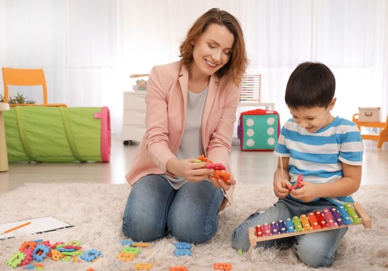 Adulto e criança brincando com xilofone e brinquedos educativos em sala colorida. Curso: Sensibilização Médicos Cooperados: Transtornos Globais do Desenvolvimento na Saúde Suplementar.