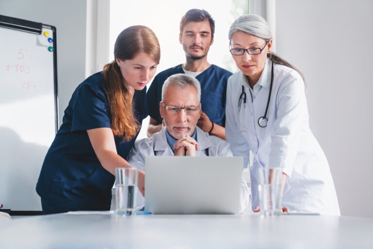 Equipe de médicos reunida à mesa analisando dados de sinistralidade em um computador em operadora de saúde.